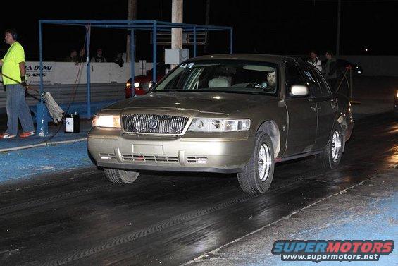 Gold Mercury Grand Marquis on drag strip, front view. Driver visible