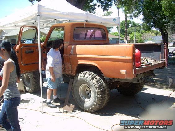 Orange pickup truck with large tires, open driver's door, and a red gas can in the bed