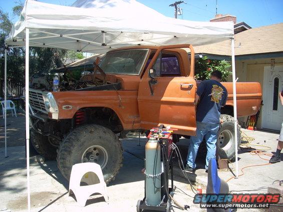 Orange pickup truck with open door and hood, being worked on