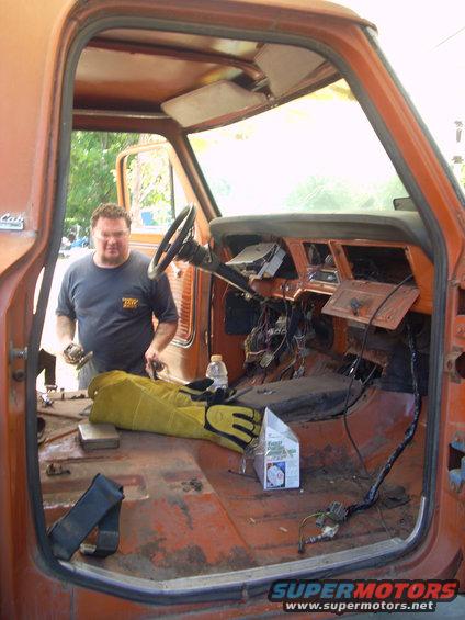 Man working on the interior of an old orange pickup truck, dash is removed, wires exposed