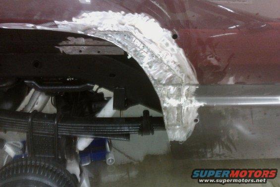 Vehicle rear wheel well with rust damage being repaired with body filler