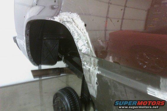 Dark red vehicle's rear wheel well and fender undergoing repair with body filler and primer