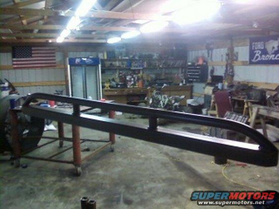 Pair of black metal rock sliders mounted on a red wheeled stand in a garage