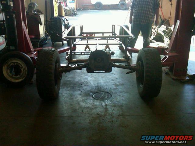 Vehicle frame with rear axle and tires on a lift in a garage