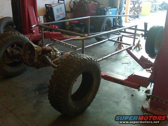 Custom tube chassis with large tires on jack stands in a garage
