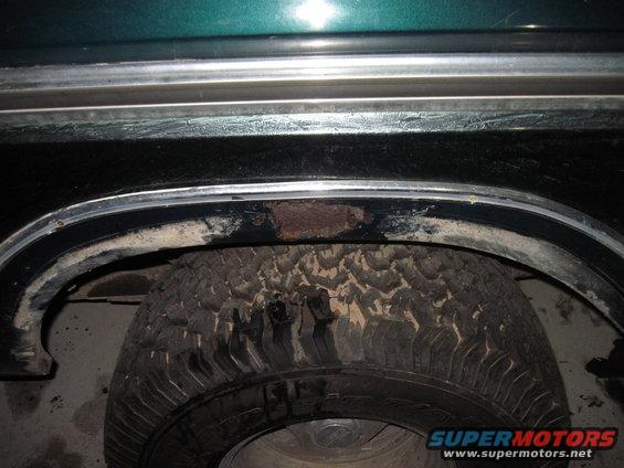 Close-up of a vehicle's rear wheel well showing a tire and some rust