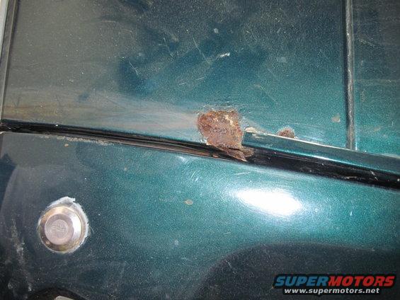 Close-up of rust forming on the edge of a green car door near a lock cylinder