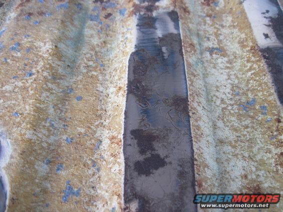 Close-up of rusted metal with blue paint flecks and a dark, textured strip