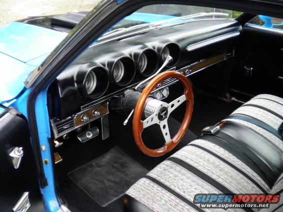 1969 Ford Ranchero interior showing dashboard with four gauges, wood steering wheel, and striped bench seat