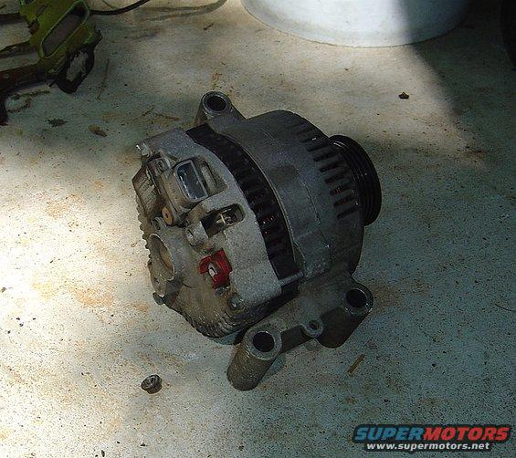 Automotive alternator with pulley and mounting brackets, resting on a concrete floor