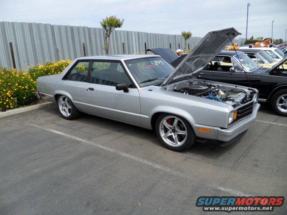 Silver coupe with hood open, aftermarket wheels, parked next to other cars