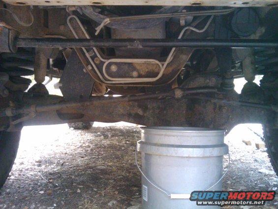 Undercarriage of a vehicle with a silver bucket underneath, showing suspension and exhaust components