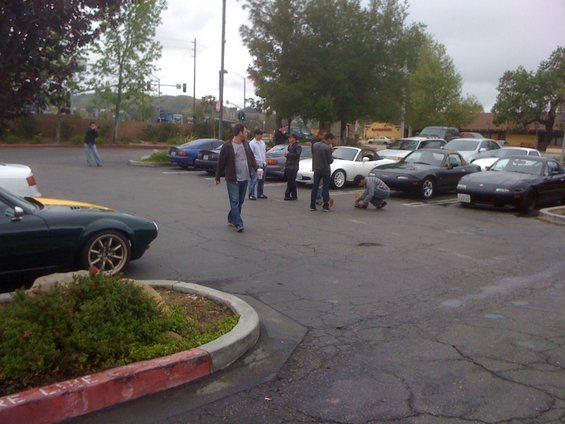 Several Mazda Miatas parked in a lot, some people standing around