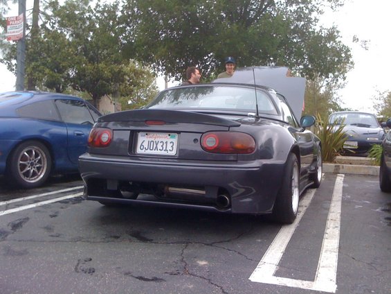 Dark gray 1991 Mazda Miata parked in a lot, hood open. Another Miata and a blue car are visible