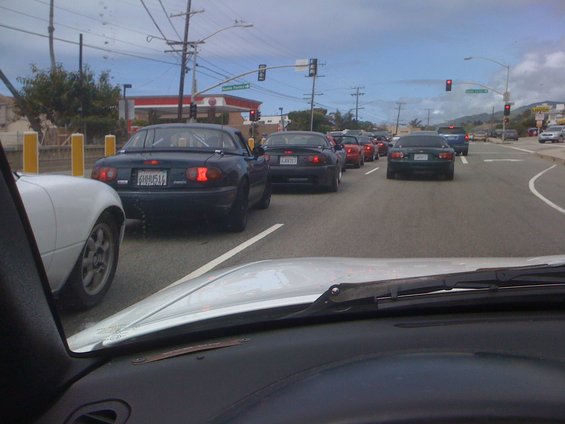 Traffic jam of dark blue Mazda Miatas on a sunny day. 1991 Mazda Miata is visible