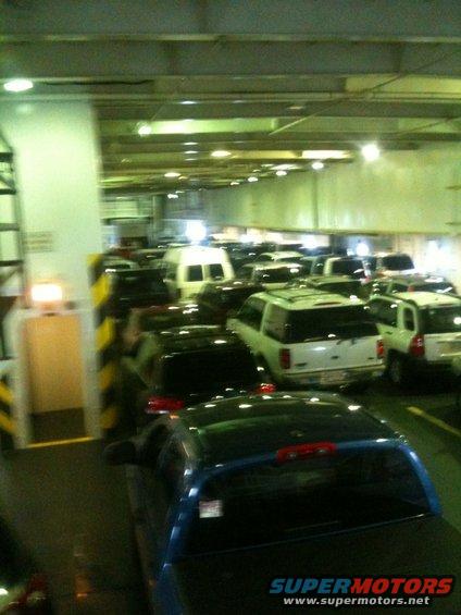 Many cars and vans parked inside a ferry. Some SUVs are visible