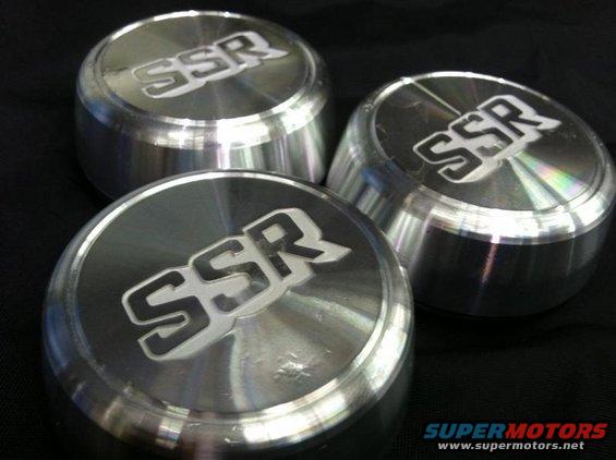 Three shiny metal SSR center caps with the SSR logo on them