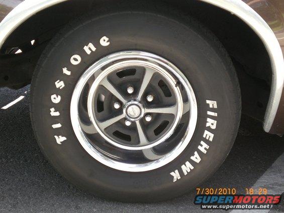 Close-up of a Firestone Firehawk tire on a car with a five-spoke chrome rim. Date stamp visible
