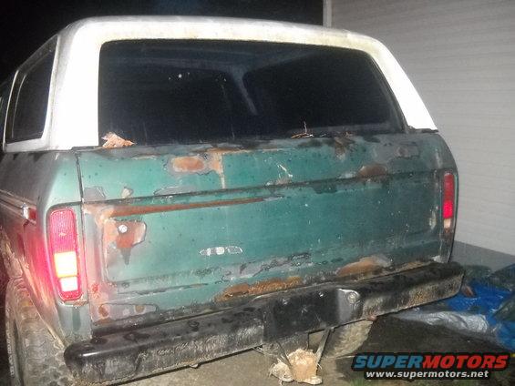Rear view of a green Ford Bronco with a white top, showing significant rust damage on the tailgate and rear quarter panels