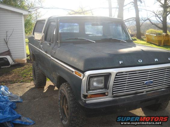 Dark blue Ford Bronco with a white top, lifted suspension, and off-road tires parked outdoors