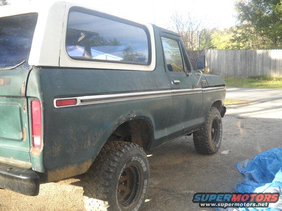 Green Ford Bronco with white top, side view. Tires are off-road style