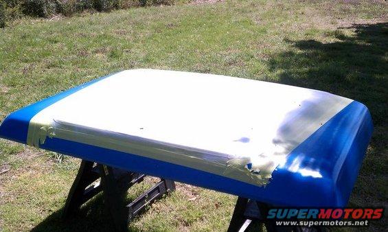 blue and white car roof panel on sawhorses, taped for painting