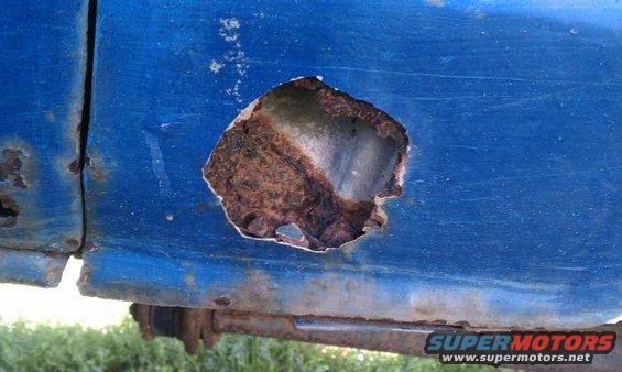 blue vehicle body with a large hole showing rust and damage