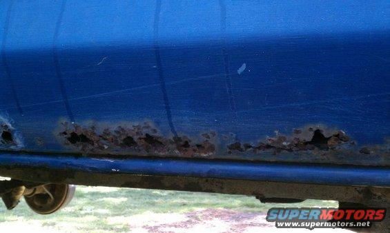 Blue vehicle lower body panel with extensive rust holes along the bottom edge