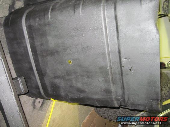underside view of a black fuel tank with a yellow wire running under it