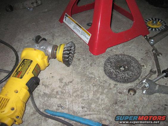 Yellow angle grinder with wire wheel attachment, cutting disc, and wrenches on concrete floor