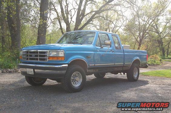 Blue 1992 Ford F-150 pickup truck, four-door cab, parked on gravel with trees in background