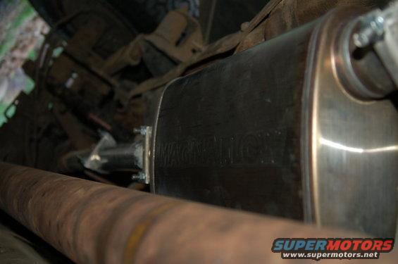 Close-up of a vehicle's exhaust muffler with visible text and a driveshaft