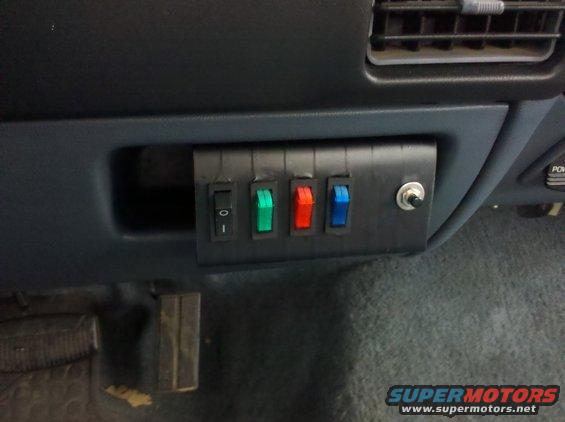 Aftermarket switch panel with four toggle switches and one push button switch mounted on a dark dashboard