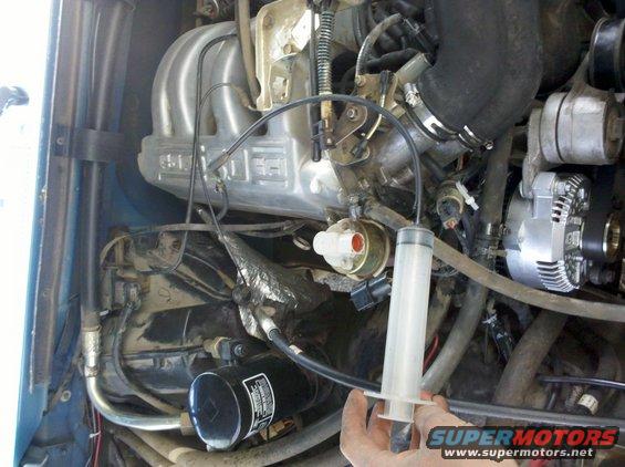 1992 Ford F-150 engine bay, close-up on the intake manifold and alternator, with a syringe in hand