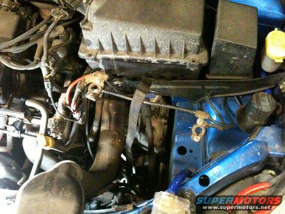 Engine bay with blue painted components, air filter housing, battery terminals, and hoses