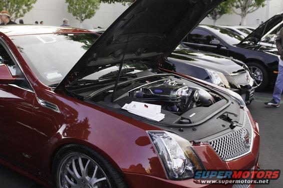 Red Cadillac sedan, hood open, showing engine. Multiple cars lined up