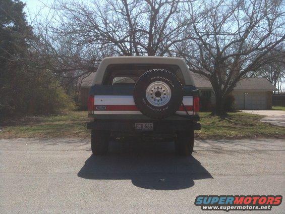 Rear view of a dark green Ford Bronco with a tan top and a spare tire on the tailgate