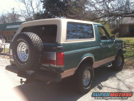 Green Ford Bronco with tan top and spare tire on back, parked outside