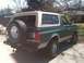 1989 Ford Bronco - This Ford Bronco is parked in front of an antique mall with trees and a house in the background.