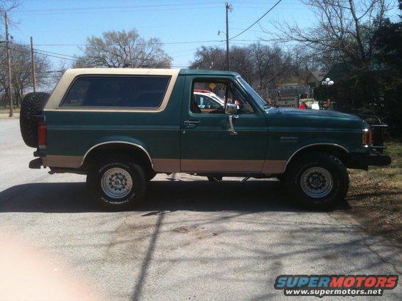 Green Ford Bronco with tan trim and a spare tire on the rear, viewed from the side