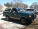 1989 Ford Bronco - This green Ford Bronco features tan lower body trim and a prominent front brush guard, seen parked on a sunny day.