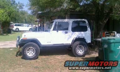 White Jeep Wrangler parked in a yard with a white van in the background