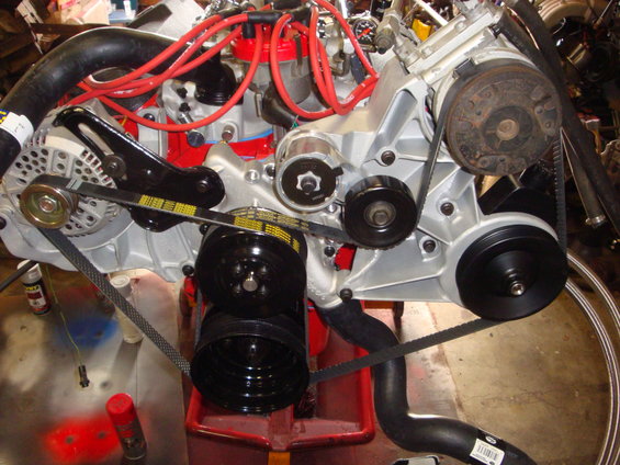 Engine block with silver finish, red spark plug wires, and black belts on pulleys
