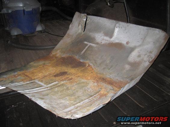 Rusted metal floor pan with a T-shaped indentation, seen from above