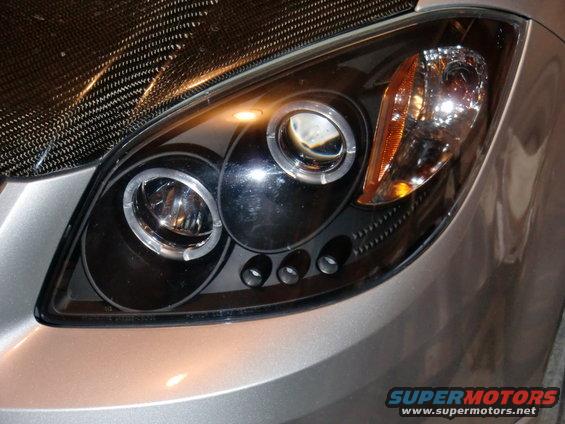 Close-up of a car's headlight assembly with a carbon fiber hood
