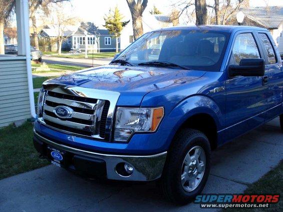 Blue Ford F-150 pickup truck, front 3/4 view, chrome grille, daytime