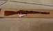 2003 Ford Crown Victoria - A rifle with a wooden stock rests on a cardboard box, with some papers underneath.
