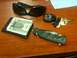 1987 Ford Bronco - A collection of personal items including sunglasses, a wallet, keys, and a knife are laid out on a wooden desk.