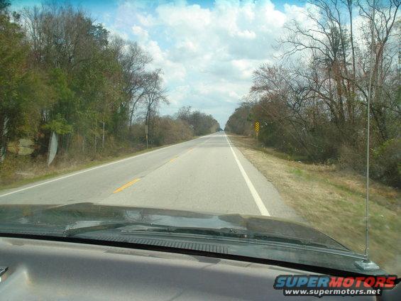 View from inside a vehicle looking out the windshield at a two-lane road with trees on both sides