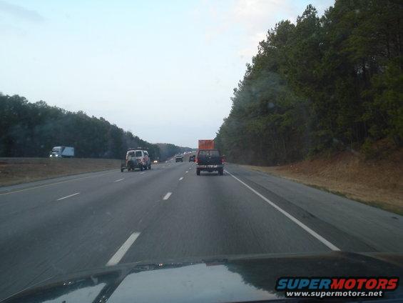 Driving on highway behind a dark pickup truck, with other vehicles and trees alongside